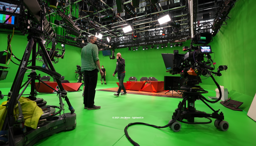 A low, wide angle view of the greenscreen studio used for the BBC's Tokyo Olympics coverage, in 2021. Designers and lighting director are in conversation, probably discussing the lighting that is being installed.